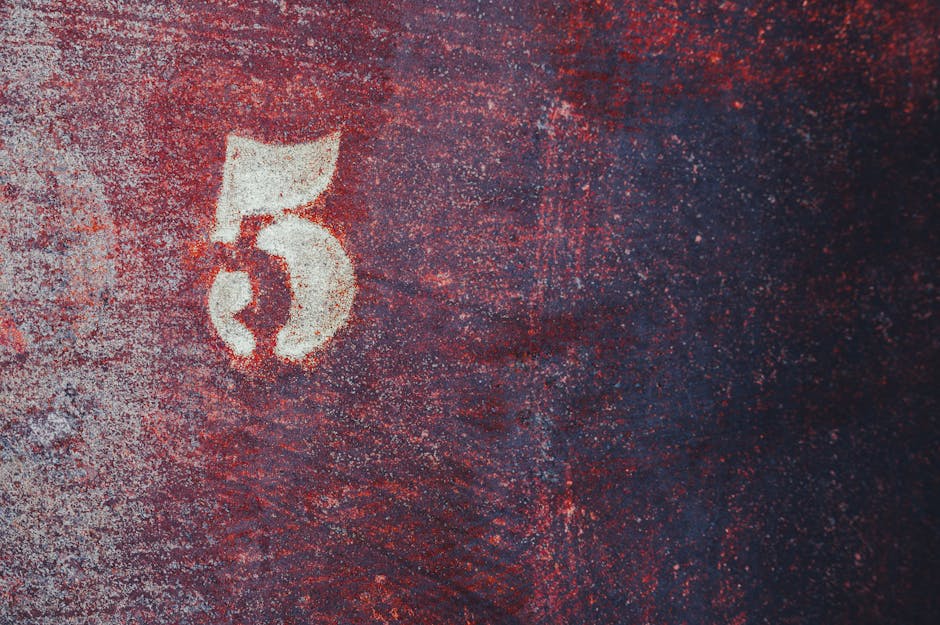 Close-up of a rusty surface with a white number five painted, demonstrating decay and texture.