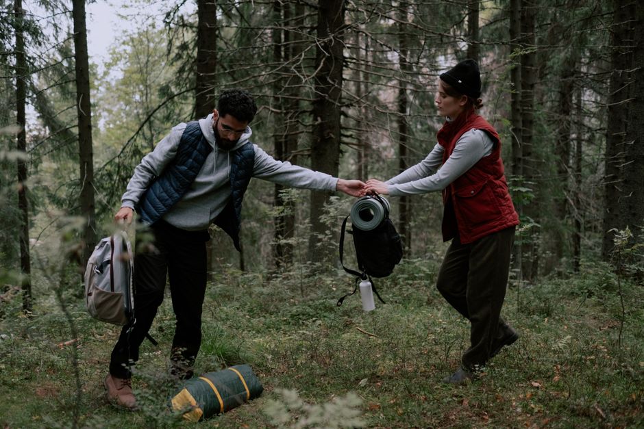 A couple prepares their campsite in a lush forest, exchanging camping gear.