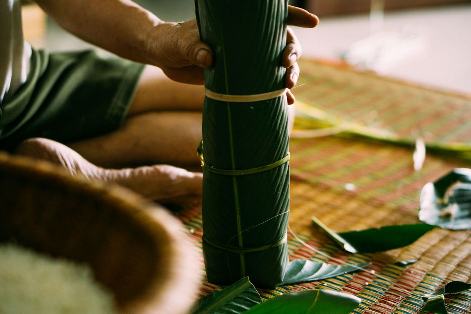 Close-up of hands wrapping leaves in traditional style on a woven mat.