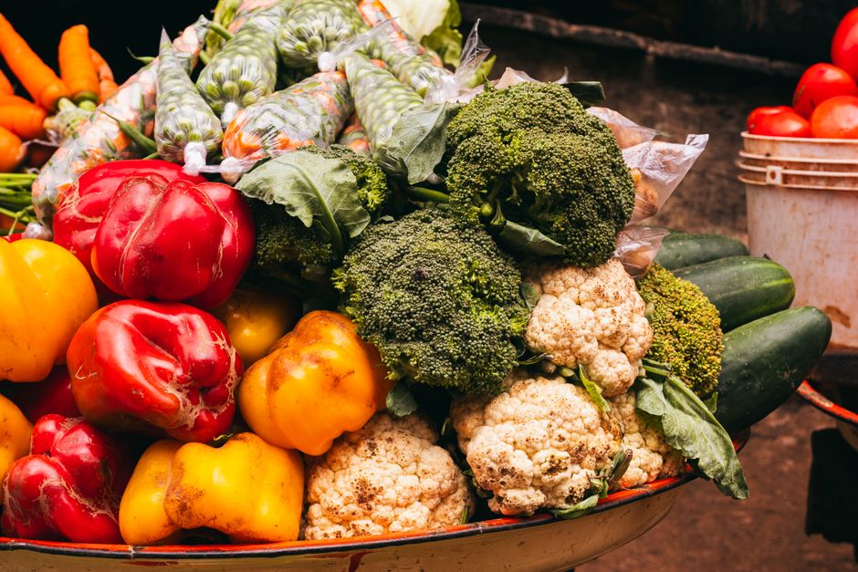 Vibrant assortment of fresh vegetables including bell peppers, broccoli, and cauliflower at a market in Nigeria.