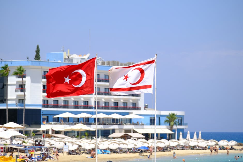 Turkish and Northern Cyprus flags waving at a coastal resort with a beach setting.