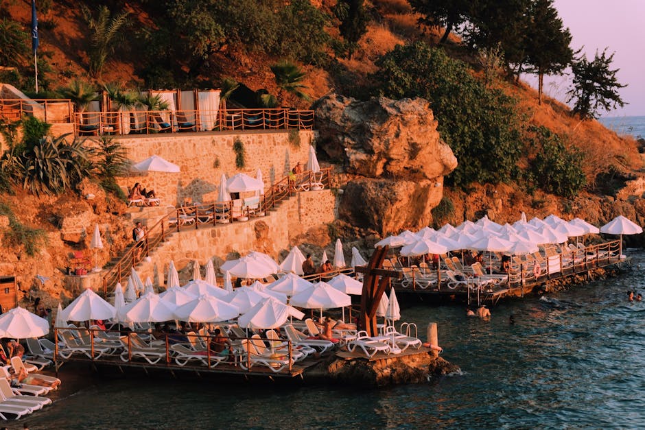 Stunning coastal resort with sun loungers and umbrellas along rocky shoreline at sunset.