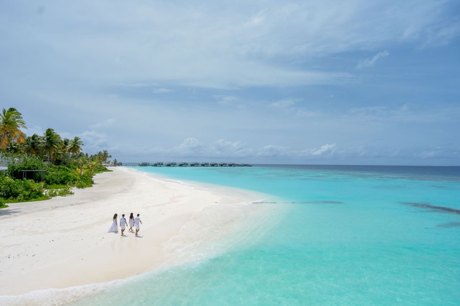 A group of people walking along a pristine tropical beach under clear blue skies.