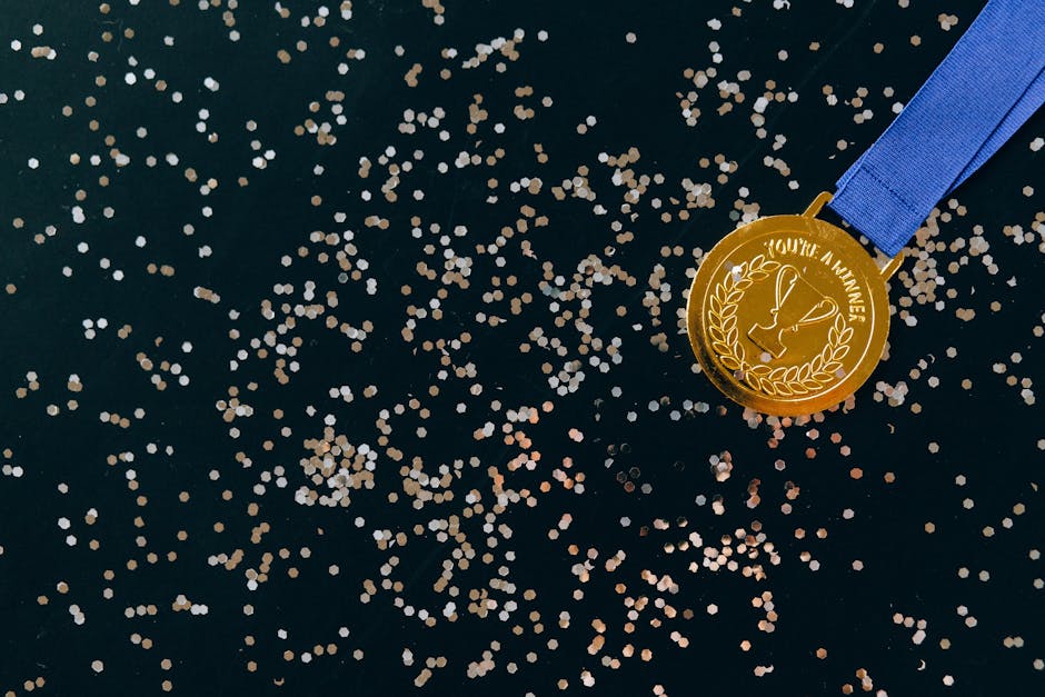 Close-up of a gold medal with blue ribbon and confetti on a black surface, symbolizing victory.