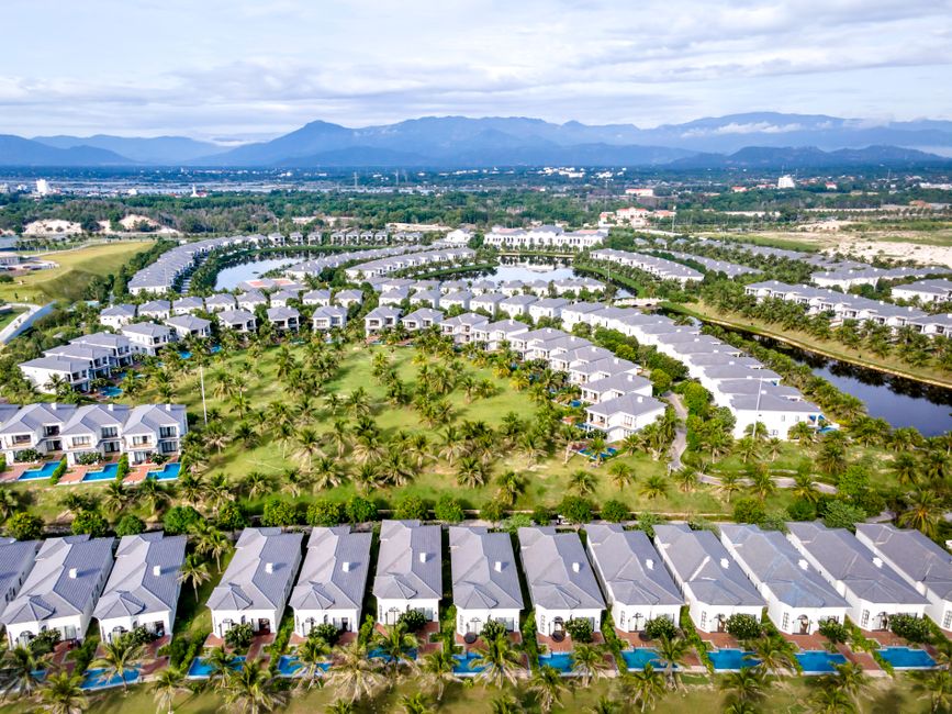 Aerial view of modern residential community with green spaces, palm trees, and blue pools.