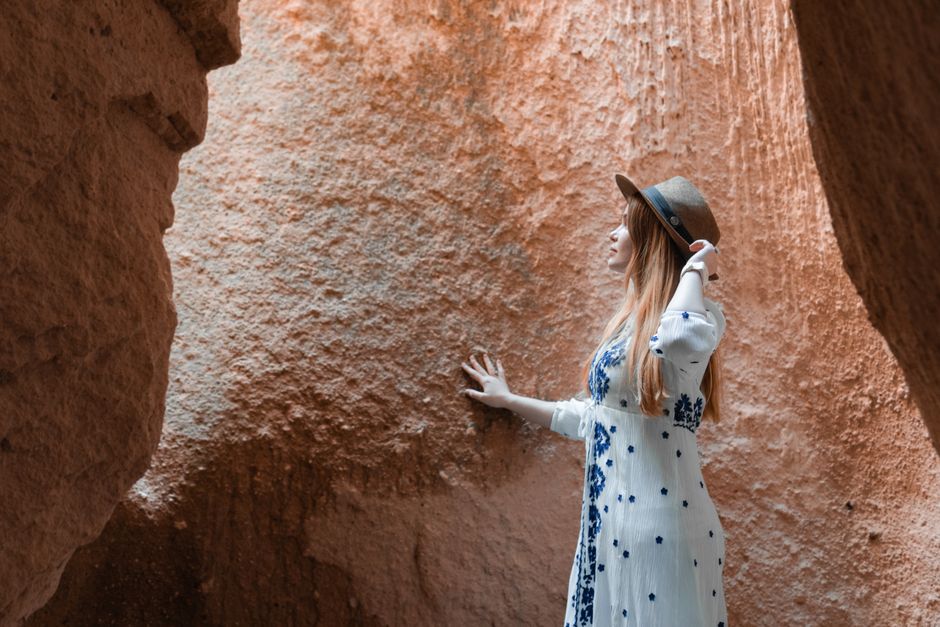 A woman in a floral dress and hat explores a cave in Türkiye, capturing a moment of adventure.