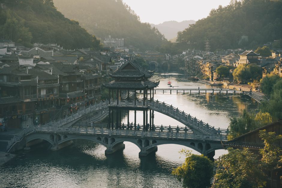 A serene sunset view over Fenghuang Ancient Town's iconic bridge and river scene.