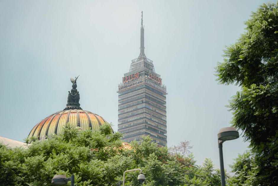 View of Torre Latinoamericana and iconic dome in Mexico City skyline with lush greenery.