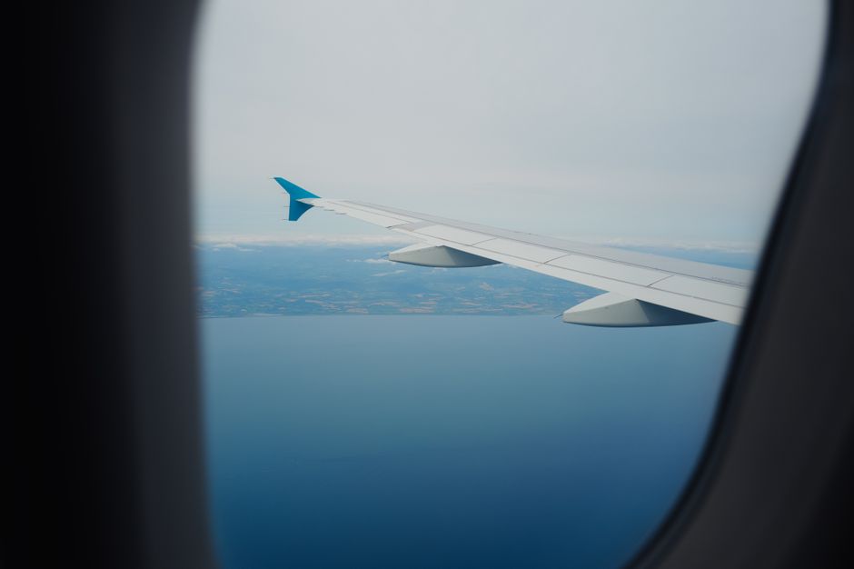 Scenic aerial view from an airplane window showing ocean and distant land below a clear sky.